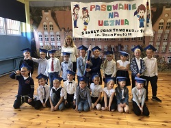 Uczniowie klasy pierwszej wraz z wychowawcą pozują na tle zdjęcia szkoły