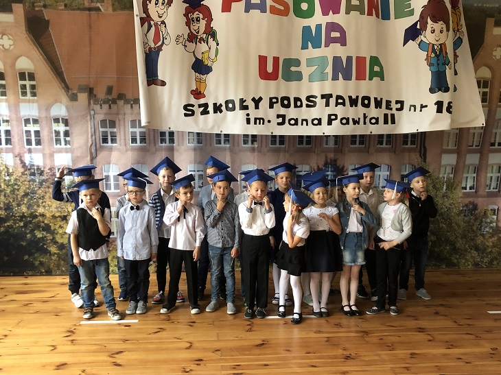 Uczniowie klasy pierwszej wraz z wychowawcą pozują na tle zdjęcia szkoły