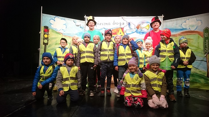 Aktoezy  dzieci pozuja do zdjęcia na scenie. Są ubrani w jaskrawe kamizelki