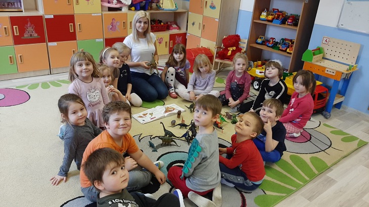 dzieci siedzą na dywanie z figurkami dinozaurów