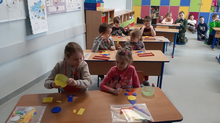 dzieci siedząc w ławkach układają pajacyka z figur geometrycznych