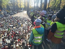 Dzieci stoją na cmentarz przy dużej ilości zapalonych zniczy