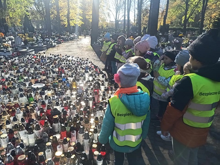 Dzieci stoją na cmentarz przy dużej ilości zapalonych zniczy