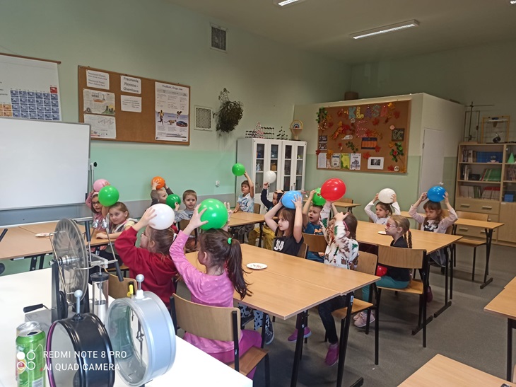 Dzieci w sali fizycznej siedzą przy stołach z balonami