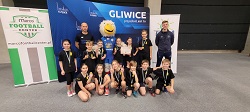 Uczniowie na spartakiadzie siedzą w rzędzie w sali gimnastycznej