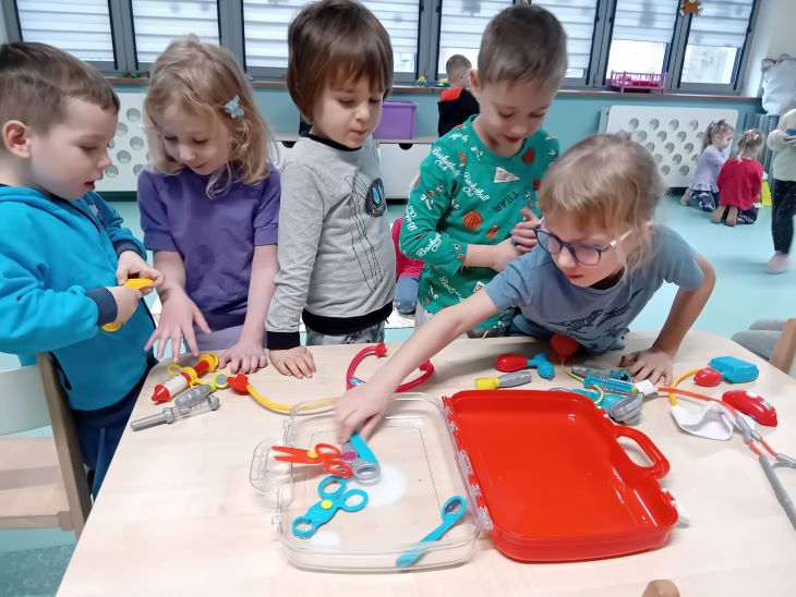 Dzieci stoją przy stoliku, na którym leżą narzędzia lekarskie