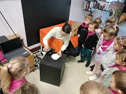 na zdjęciu Dzieci przyglądają się przeprowadzanemu przez pracownika muzeum eksperymentowi, pokazującemu reakcję na zetknięcie się tłuszczu i wody.