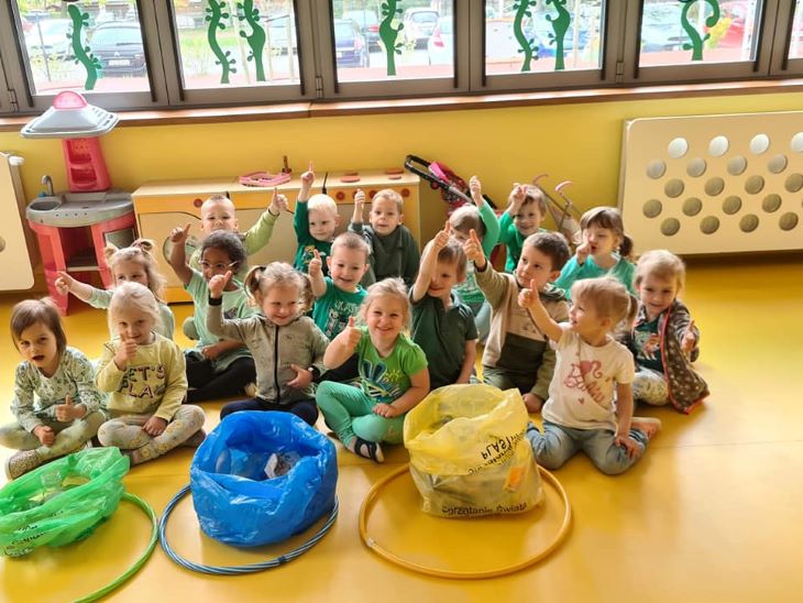 Dzieci siedzą w sali, a obok nich leżą posegregowane śmieci w odpowiednich workach.