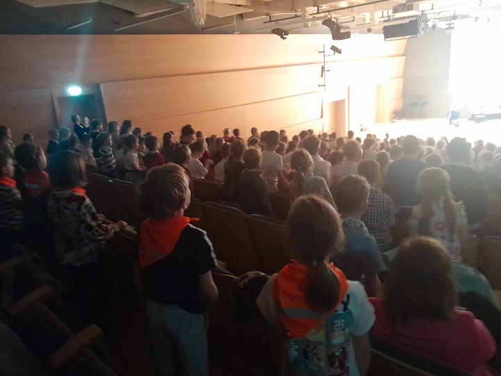 na zdjęciu dzieci stoją w sali koncertowej patrząc na scenę