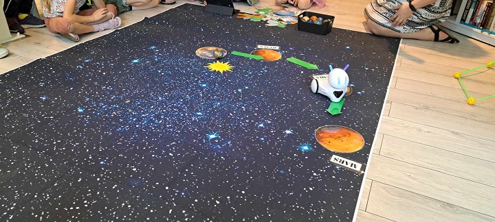 na zdjęciu grupa dzieci pozuje w Bibliotece, przed nimi stoi jedno dziecko przebrane za astronautę