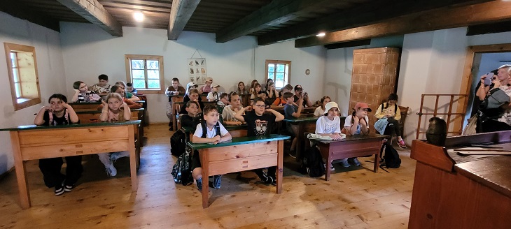 wycieczka do parku etnograficznego klas trzecich, uczniowie siedza w zabytkowej szkole w starych ławkach