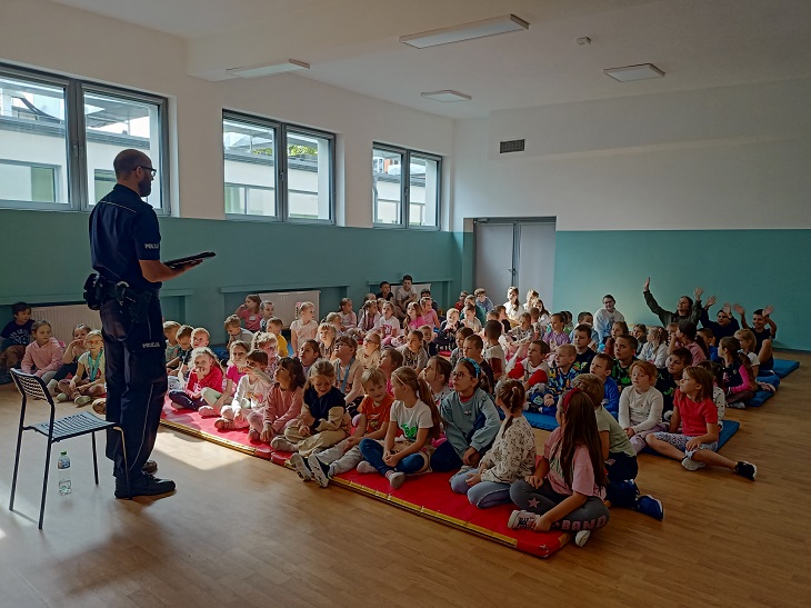 Policjant mówi do dzieci w czasie spotkania edukacyjnymi z uczniami w klasie 1