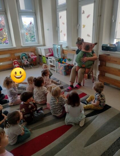 nauczycielka z maskotką otoczona gromadką dzieci siedzących na podłodze