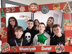 Na zdjęciu znajduje się grupa uczniów pozujących do wspólnej fotografii w świątecznej dekoracji z napisem „Wesołych Świąt”. Fotografia została wykonana w szkolnej sali i oddaje radosną, świąteczną atmosferę.