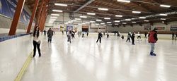 Na zdjęciu widać dużą halę lodowiska, na którego tafli jednocześnie jeździ wiele osób. Uczniowie poruszają się po lodzie w różnych kierunkach, część z nich jeździ samodzielnie, inni w mniejszych grupach. Widoczna jest aktywność i ruch, a cała scena oddaje atmosferę wspólnej zabawy oraz sportowego wysiłku.  Lodowisko jest przestronne i dobrze oświetlone, a bandy oraz konstrukcja hali wskazują na obiekt miejski przystosowany do zajęć rekreacyjnych. Zdjęcie pokazuje radosny, aktywny charakter wyjścia szkolnego i czas spędzony na świeżej aktywności.
