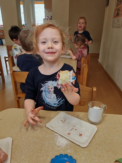 uśmiechnięta dziewczynka z papierowym pączkiem pomalowanym farbą