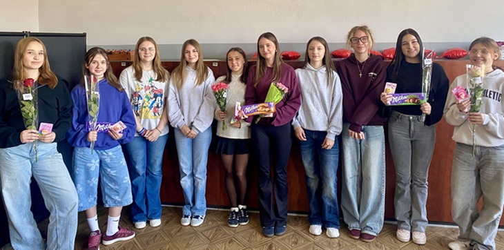 Na zdjęciu widać grupę uczennic stojących obok siebie w szkolnej sali. Dziewczynki trzymają w rękach róże oraz drobne upominki, które otrzymały podczas szkolnego konkursu „Dama Szkoły”. Uczestniczki uśmiechają się do zdjęcia, a fotografia upamiętnia wspólną zabawę i udział w konkursie zorganizowanym z okazji Dnia Kobiet.
