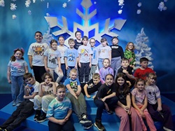 Na zdjęciu widać grupę dzieci z klas 2 podczas wycieczki do Funzeum. Uczniowie stoją i siedzą razem na niebieskich stopniach, pozując do wspólnego zdjęcia. W tle znajduje się duża, dekoracyjna śnieżynka oraz zimowa scenografia z niebieskim tłem i ozdobami przypominającymi śnieg. Dzieci wyglądają na zadowolone i uśmiechnięte, co pokazuje, że wycieczka była dla nich radosnym przeżyciem.