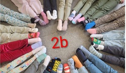 Uczniowie klasy 2b siedzą w kręgu, prezentując kolorowe, niepasujące do siebie skarpetki. Zdjęcie symbolizuje różnorodność, jedność oraz wspólne zaangażowanie w akcję.