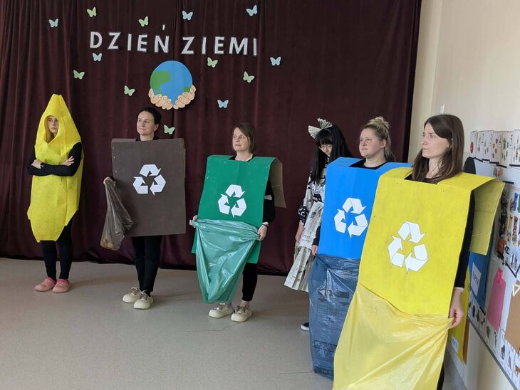 nauczycielki stojące na środku sali, przebrane w kartonowe stroje imitujące kontenery na śmieci