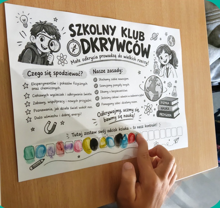 Na zdjęciu widać kartę informacyjną Szkolnego Klubu Odkrywców. Karta znajduje się na ławce, a dziecko wskazuje palcem jeden z jej elementów.  Na plakacie przedstawiono kolorowe, dziecięce ilustracje związane z nauką i odkrywaniem świata, m.in. lupę, żarówkę, probówki oraz postacie młodych odkrywców. Znajdują się na nim również informacje dotyczące działalności Klubu, między innymi tego, czego uczniowie będą poszukiwać i jakie zasady będą obowiązywać podczas zajęć.  Zdjęcie pokazuje ciekawą i angażującą formę zaprezentowania dzieciom zajęć przyrodniczych, zachęcającą je do eksperymentowania, zadawania pytań i odkrywania świata.