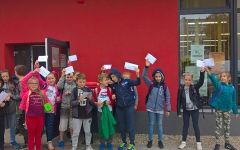 Uczniowie stoja przed budynkiem Biblioteki Miejskiej i trzymają w rękach listy